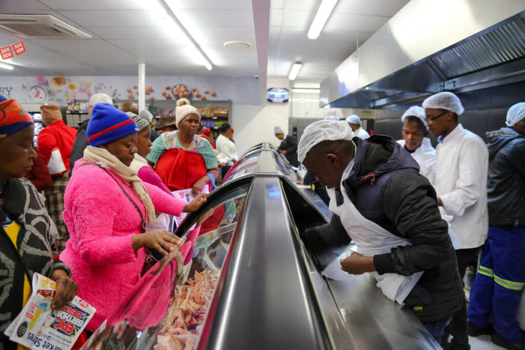 Vitrine de alimentos refrigerados rodeada por consumidores e atendentes de supermercado em Joanesburgo, na África do Sul | Foto: Africanstar/Shutterstock